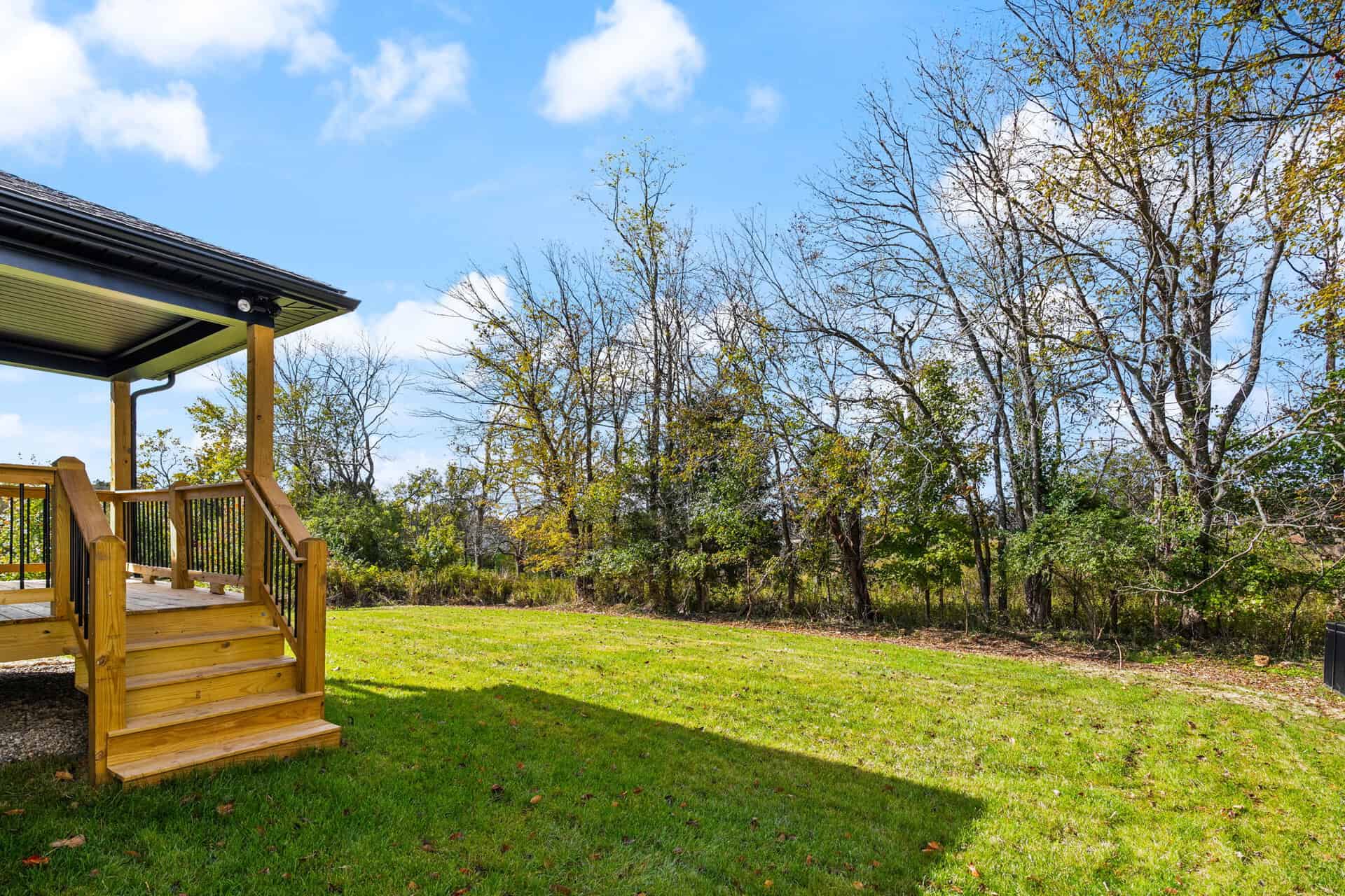 Spacious backyard with green grass, trees, and a wooden deck in Louisville, KY.