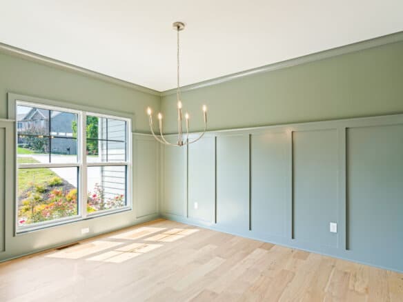 Bright empty room with large window, chandelier, and light green walls.