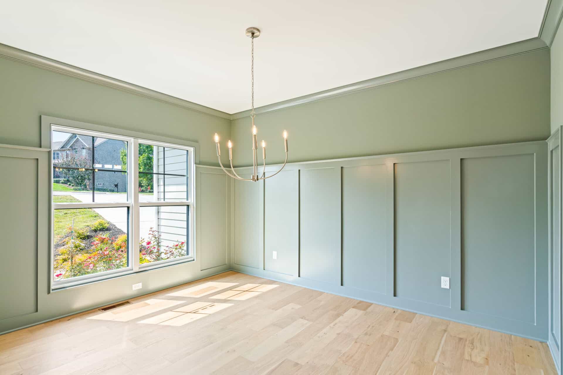 Bright empty room with large window, chandelier, and light green walls.