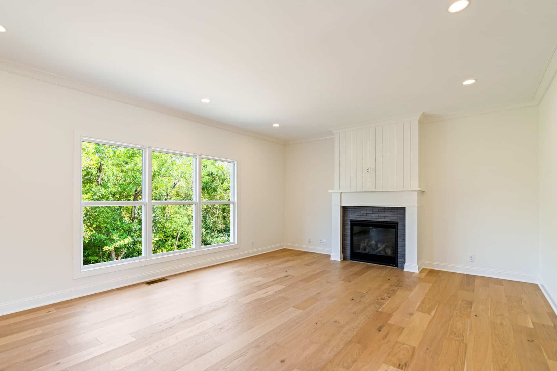 Bright living room with large window, white walls, and wood flooring.
