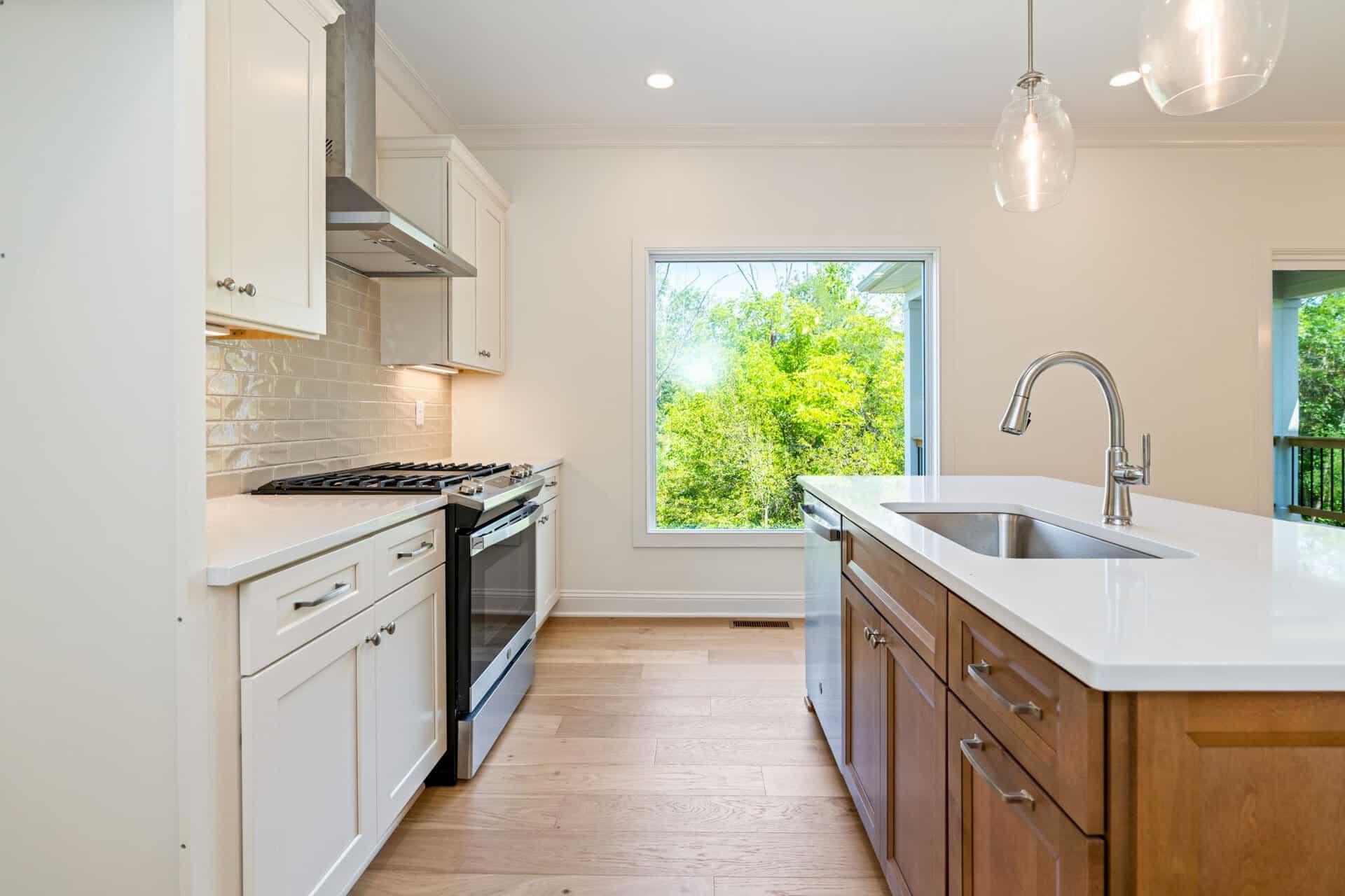 Modern kitchen with white cabinets, wooden island, and large windows showing greenery.
