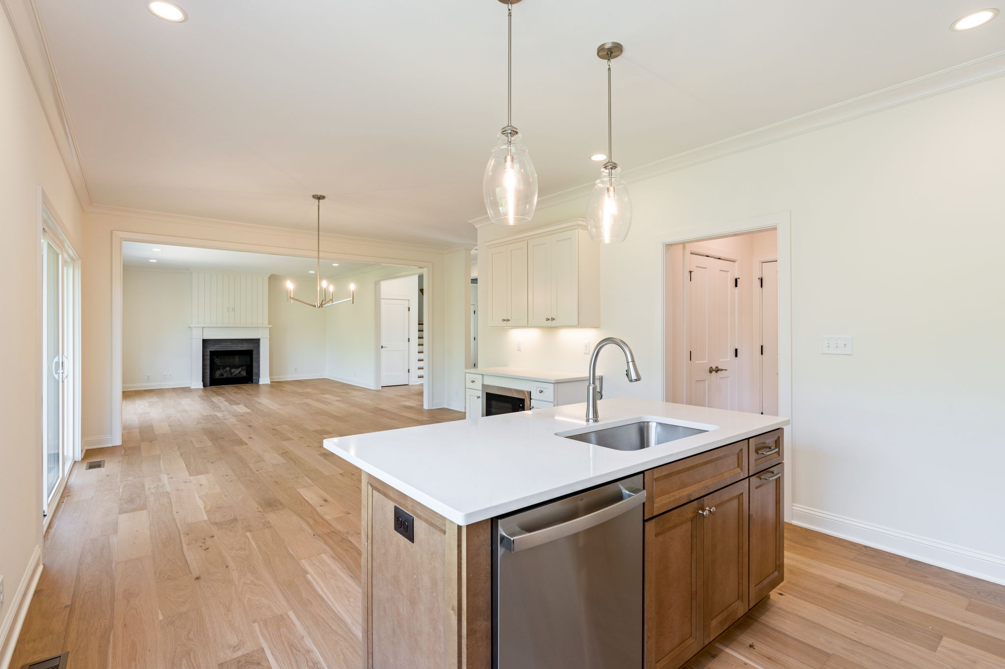 Open-concept kitchen with an island, glass pendant lights, white cabinets, and a view of the living room with a fireplace in the background.