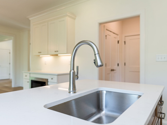 Close-up of a stainless steel kitchen faucet over a white island sink in a bright kitchen.