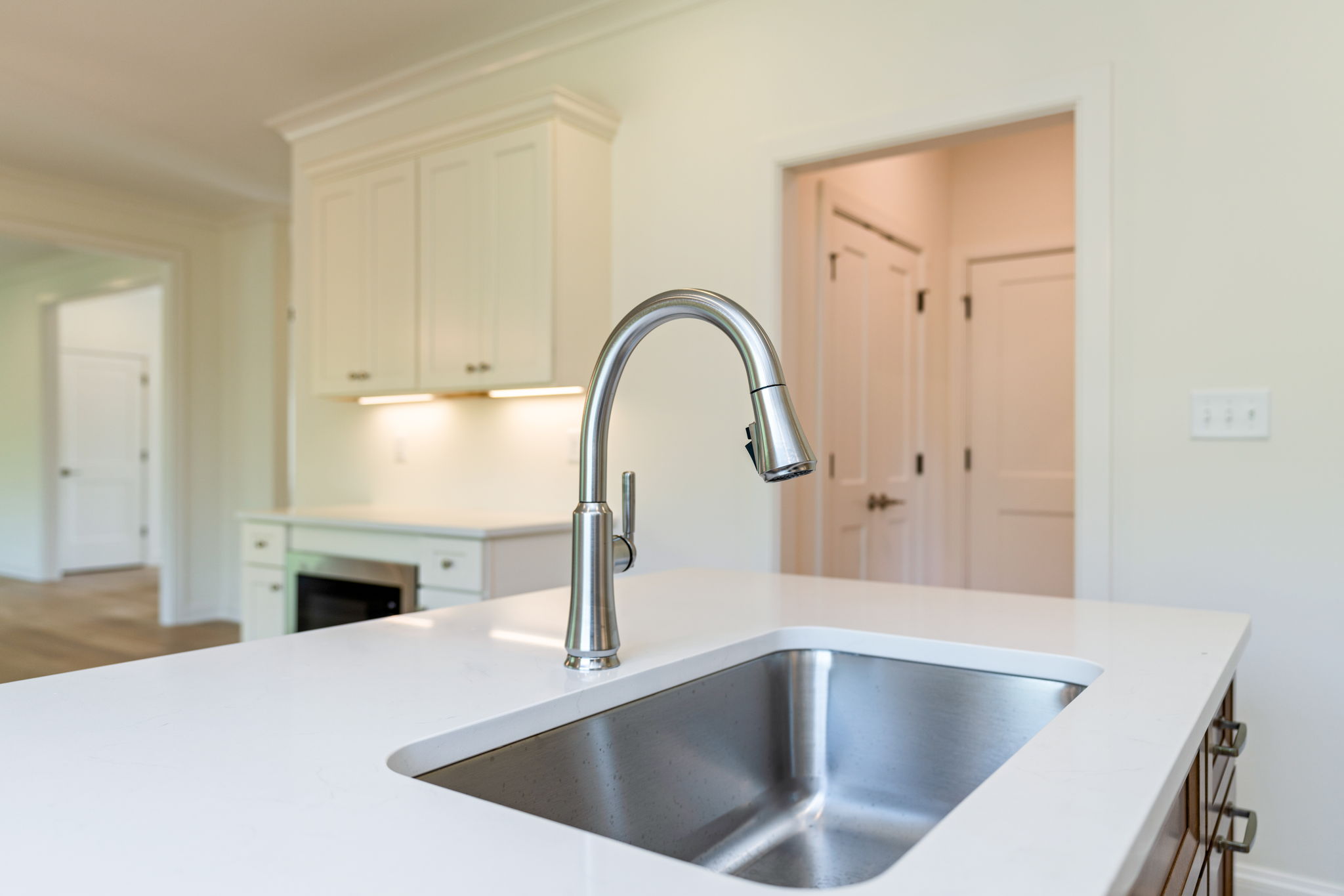 Close-up of a stainless steel kitchen faucet over a white island sink in a bright kitchen.