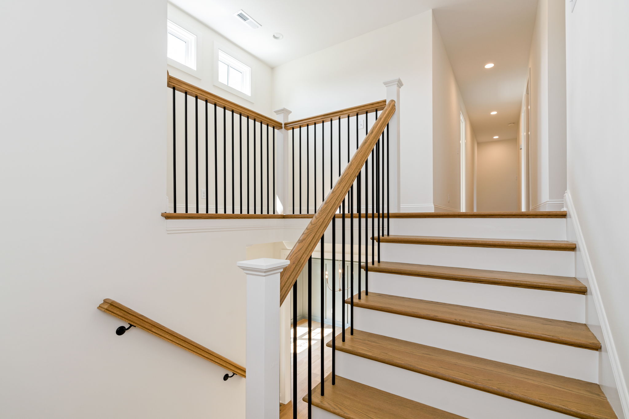 Interior staircase with wooden steps and black metal balusters along white walls in a bright hallway.