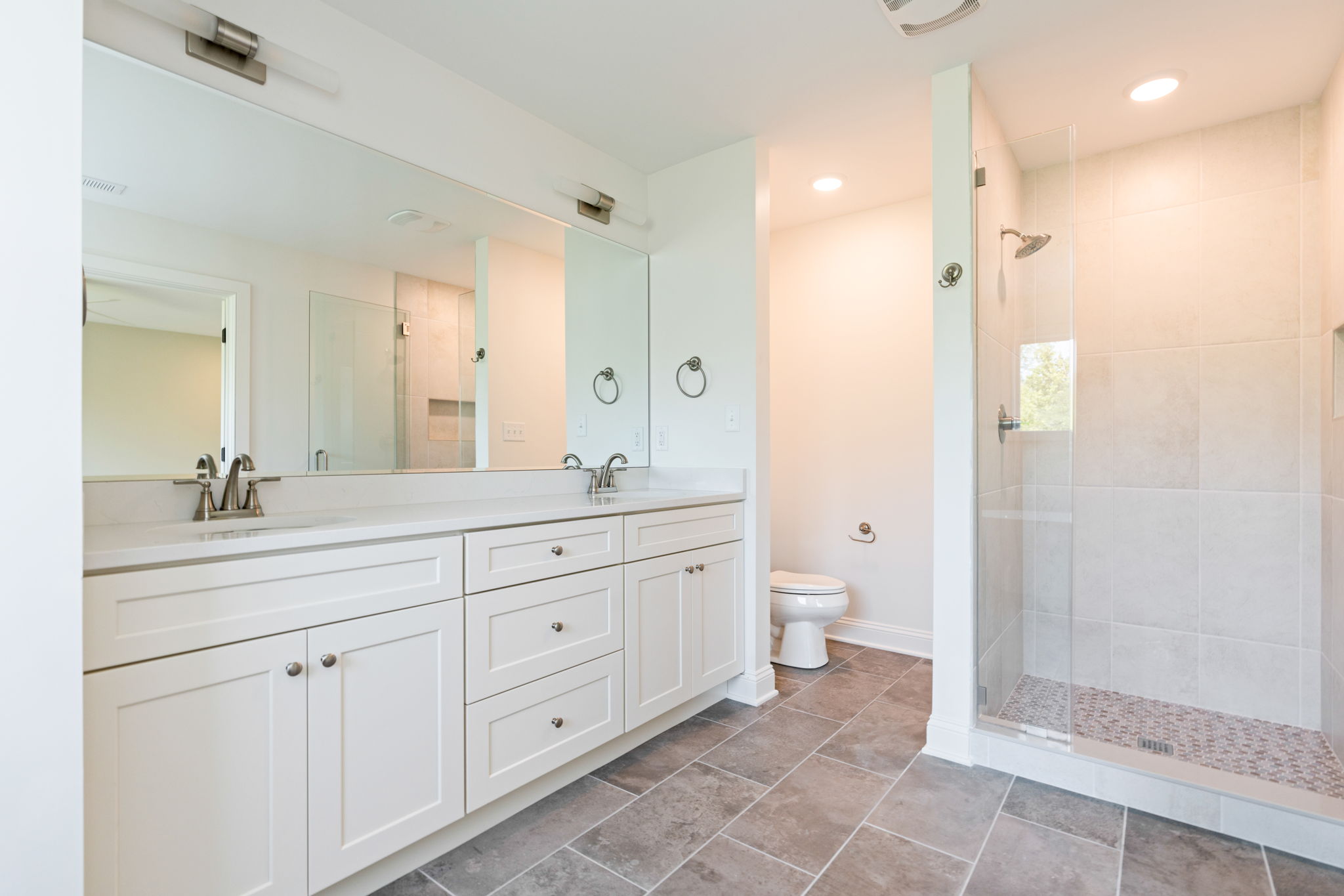 Bright modern bathroom with a white double-sink vanity, large mirror, and glass-enclosed shower.
