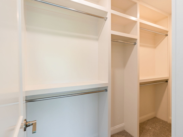 Open walk-in closet with white built-in shelves and metal clothing rods