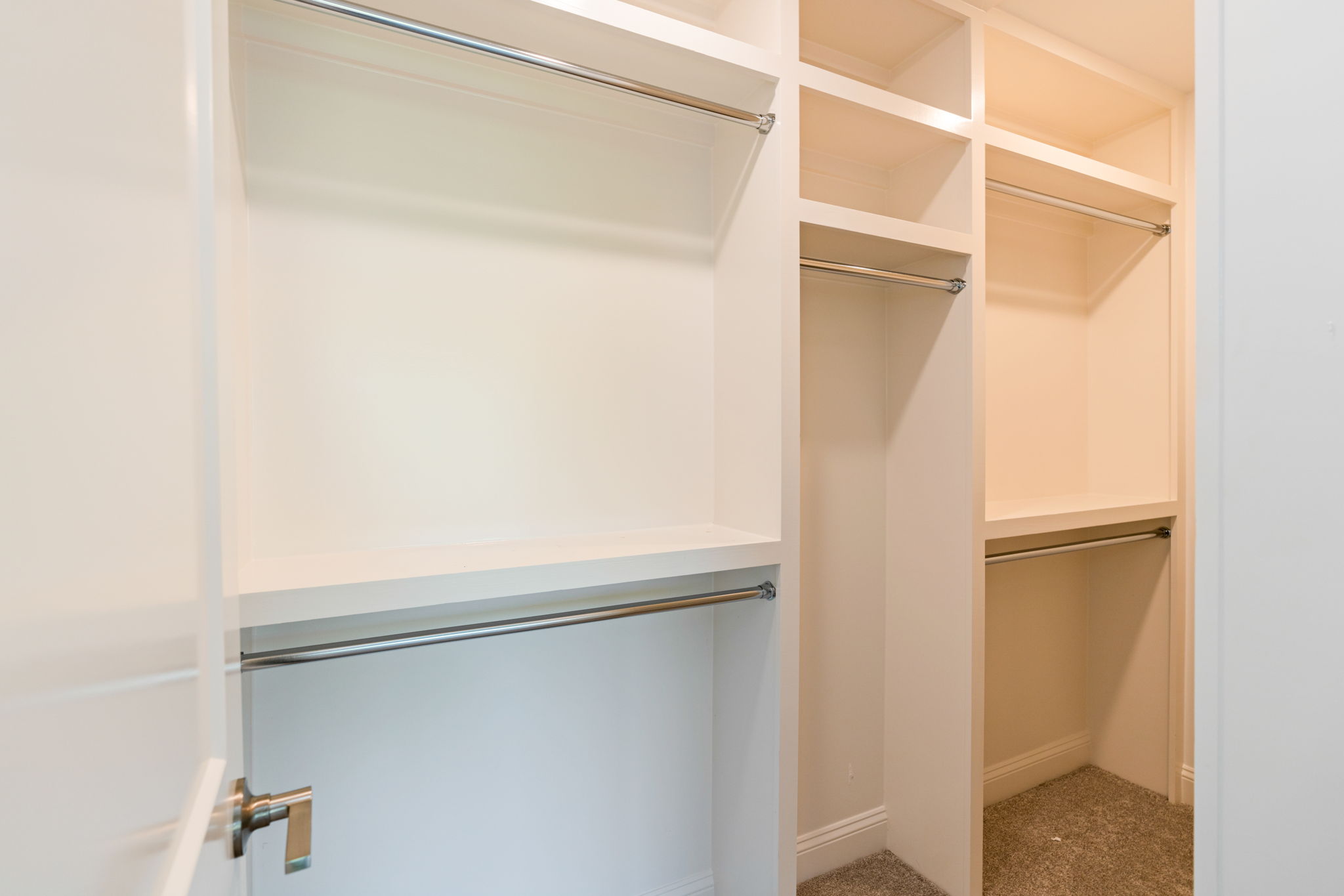 Open walk-in closet with white built-in shelves and metal clothing rods