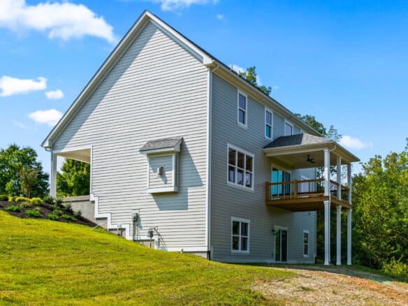 Modern white house with a wooden balcony on a grassy hill under a blue sky.