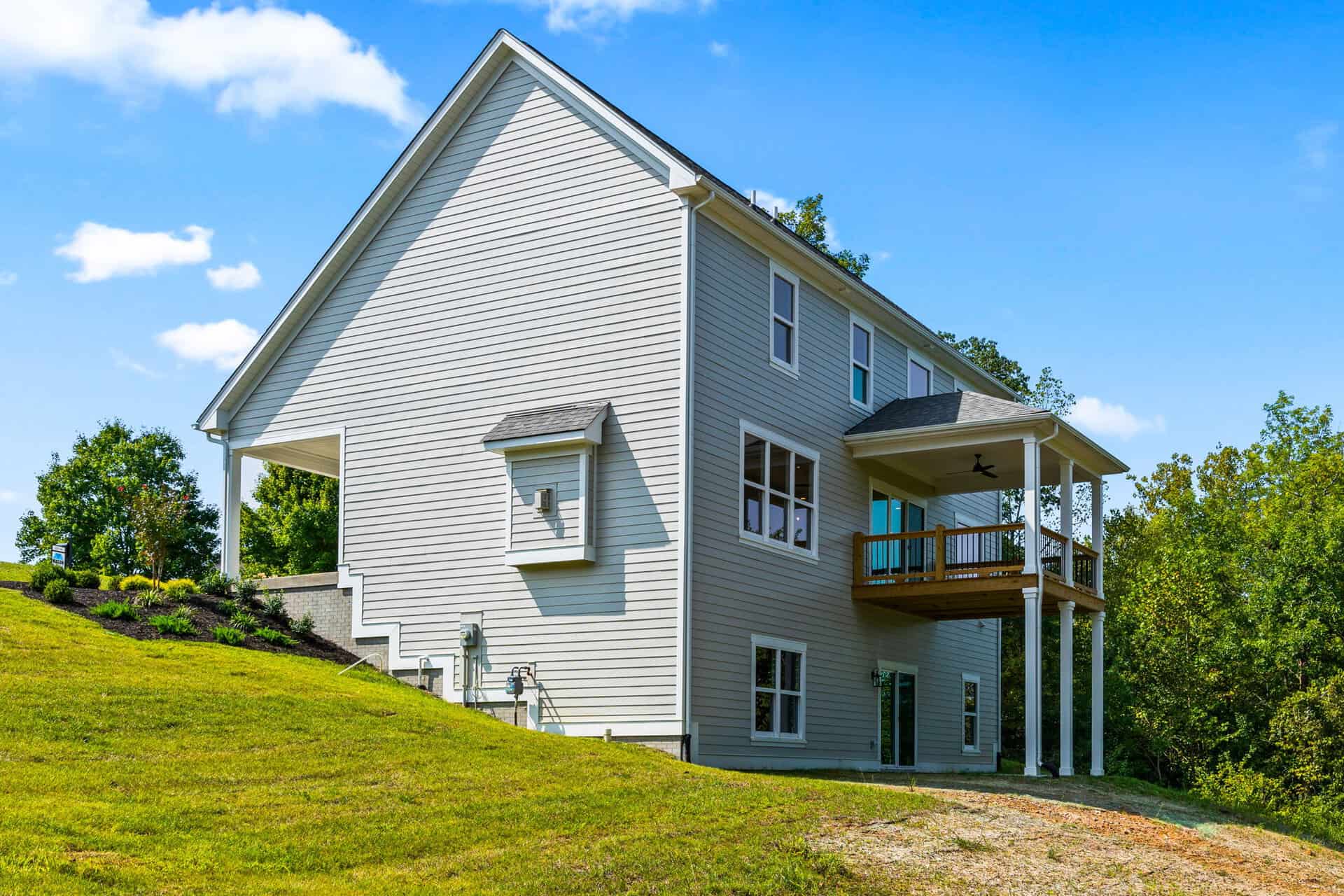 Modern white house with a wooden balcony on a grassy hill under a blue sky.