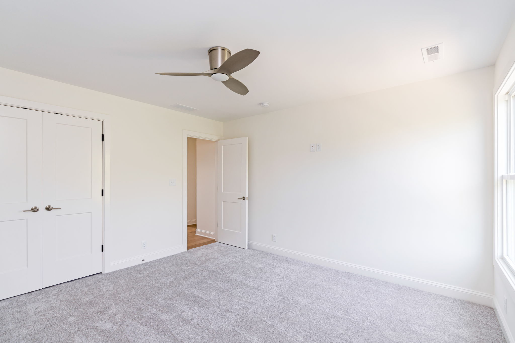 Unfurnished bedroom with white doors, light gray carpet, and a modern ceiling fan.
