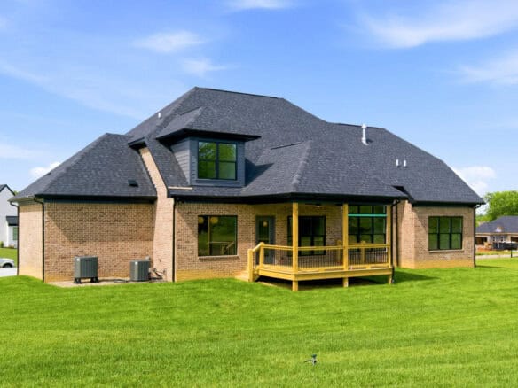 Modern brick house with a large backyard and a wooden deck under a blue sky.