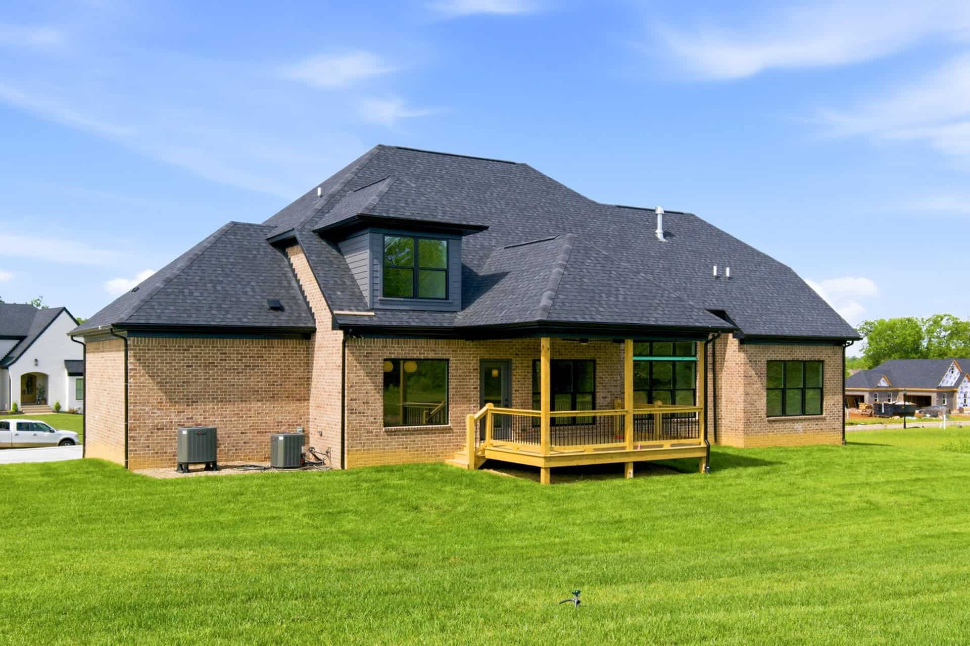 Modern brick house with a large backyard and a wooden deck under a blue sky.