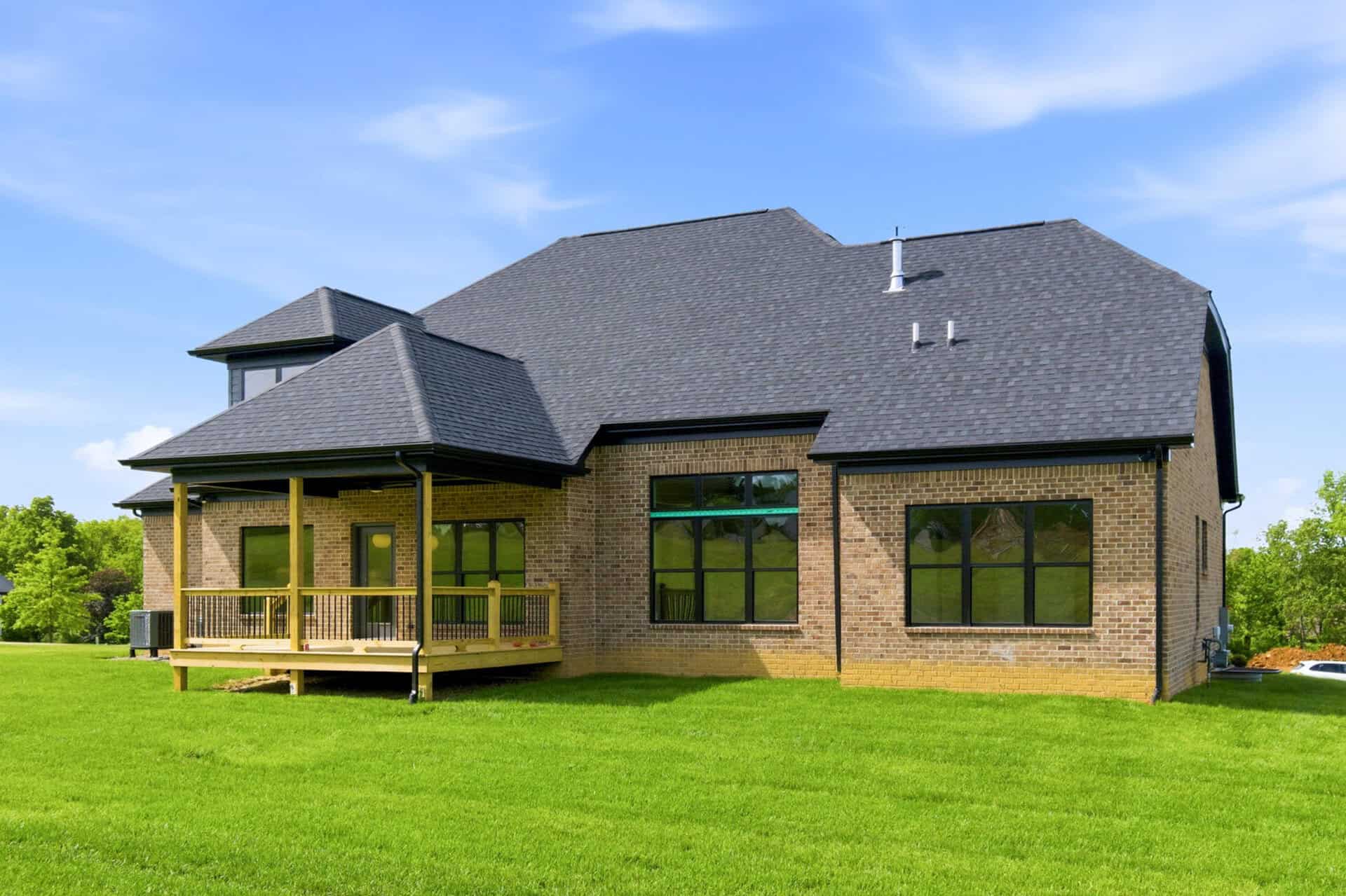 Modern brick home with a spacious wooden deck and green lawn.