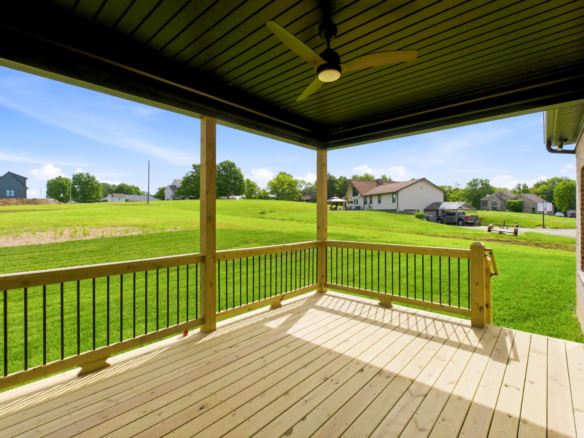 Wooden deck under a dark ceiling with a ceiling fan, overlooking a green suburban yard and houses in the distance.