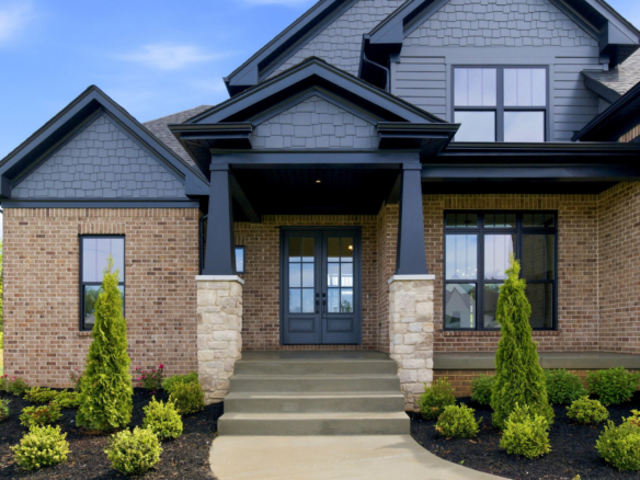 Front porch of a brick house with grey siding, black-framed windows, and stone columns supporting a covered entryway.