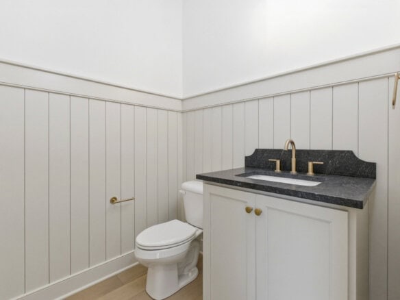 Clean white bathroom with a black countertop and gold fixtures.
