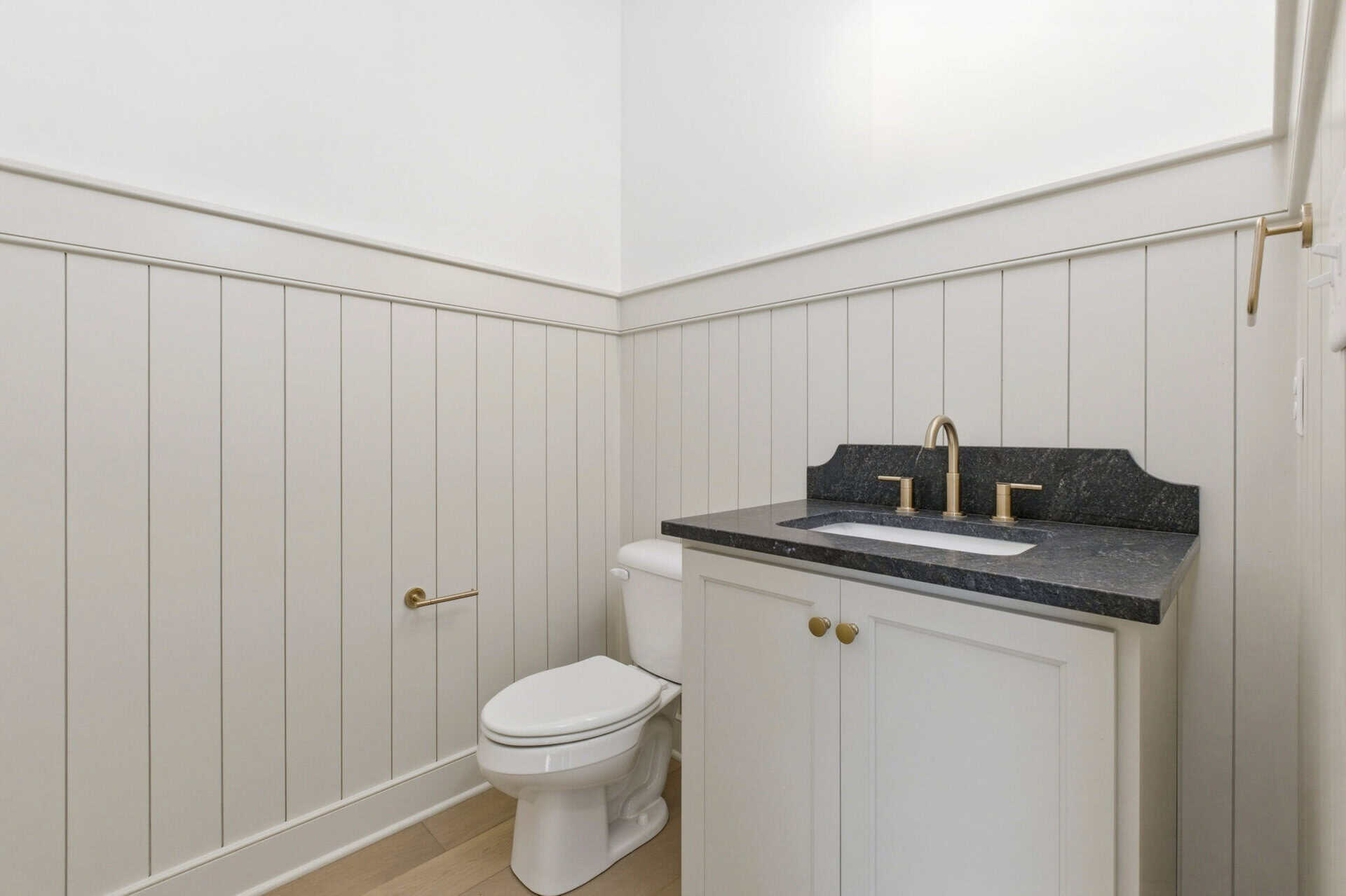 Clean white bathroom with a black countertop and gold fixtures.