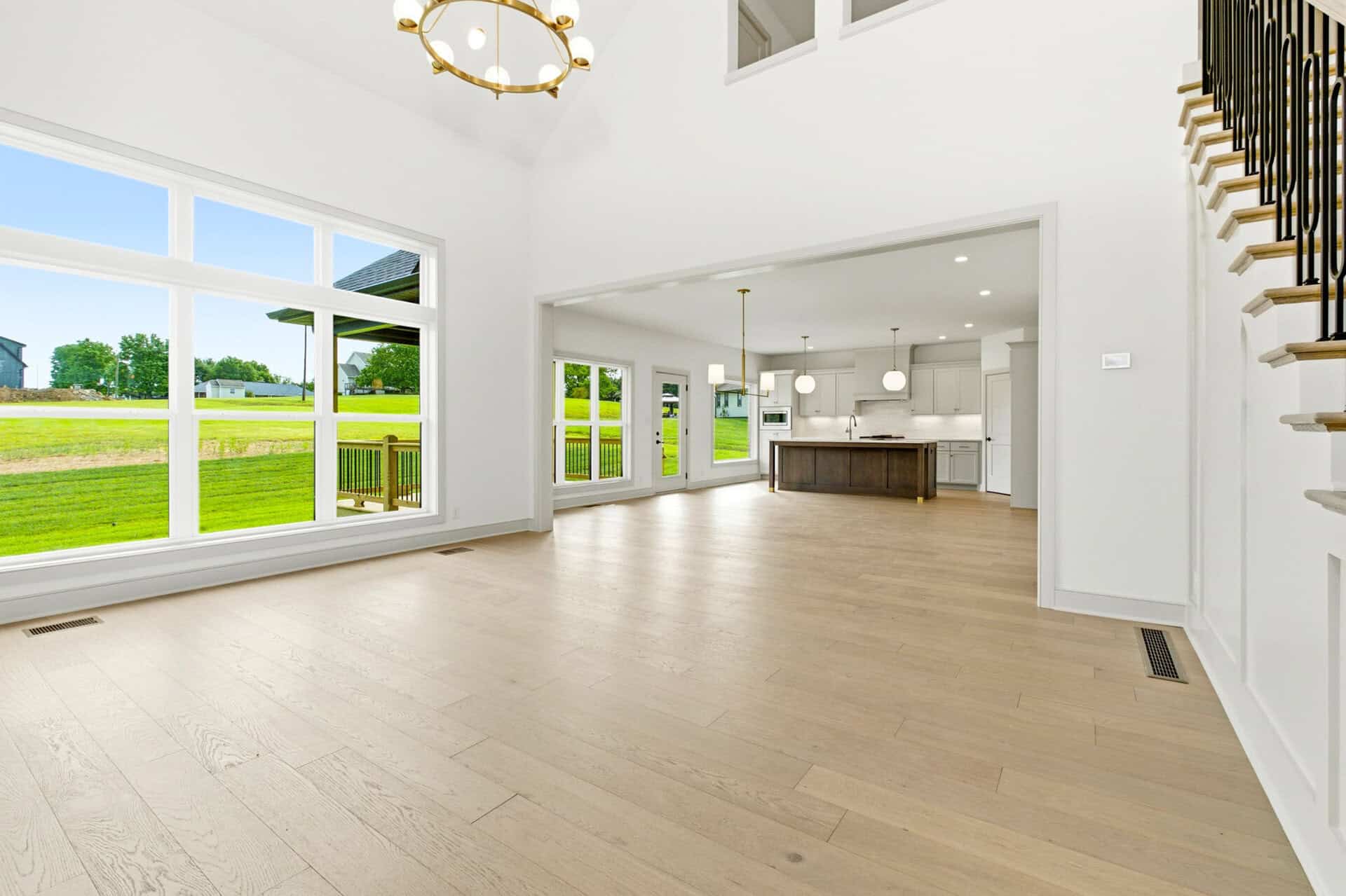 Bright open-concept living area with large window walls, white walls, and a central kitchen island visible in a spacious home interior