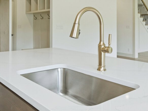 Brass kitchen faucet arches over a white quartz island sink in a bright modern kitchen.