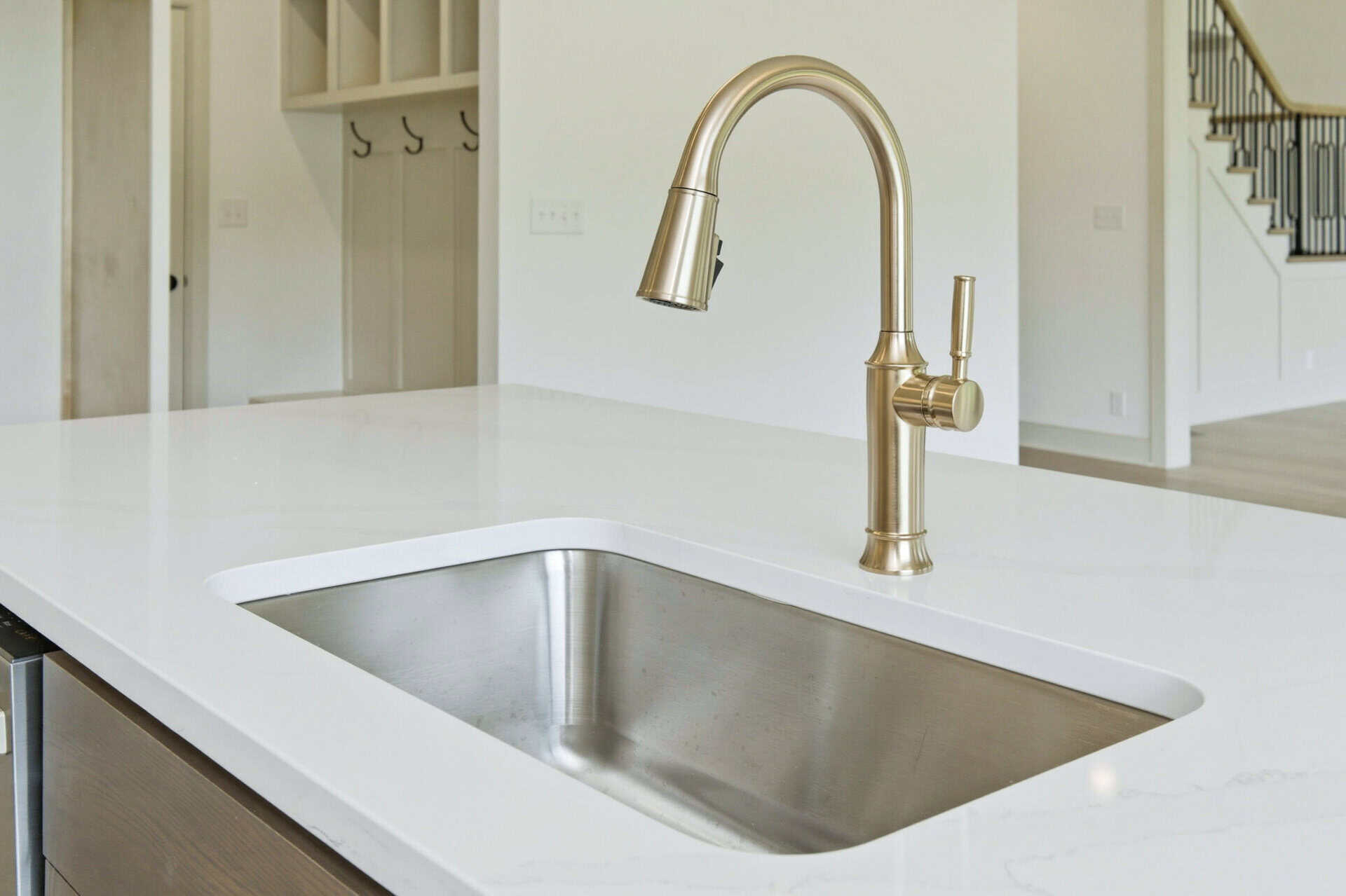 Brass kitchen faucet arches over a white quartz island sink in a bright modern kitchen.