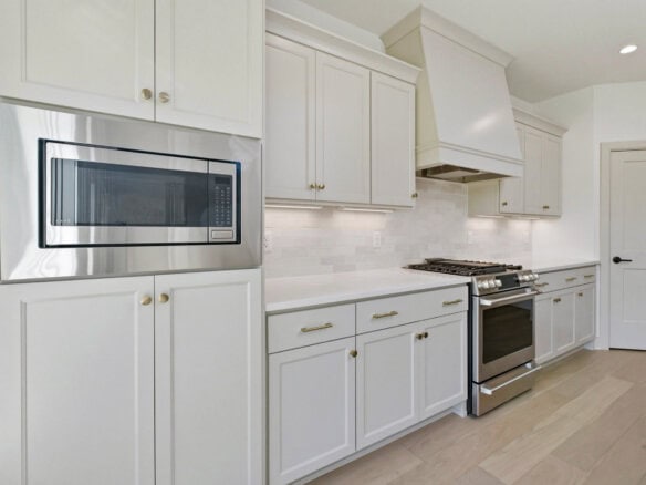 Modern kitchen with white cabinets and stainless steel microwave above a gas range, light backsplash and hood.