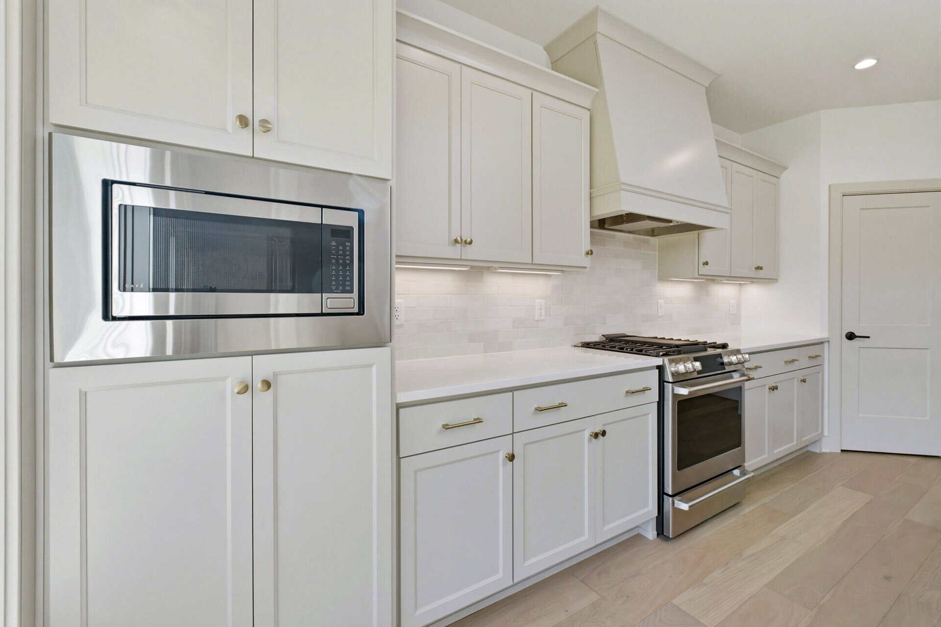 Modern kitchen with white cabinets and stainless steel microwave above a gas range, light backsplash and hood.