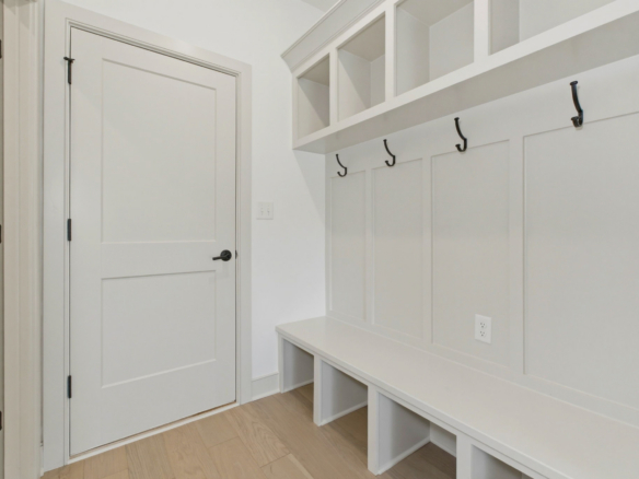 White entry nook with a built-in bench, beadboard wall, five coat hooks, and wall cubbies above the bench.