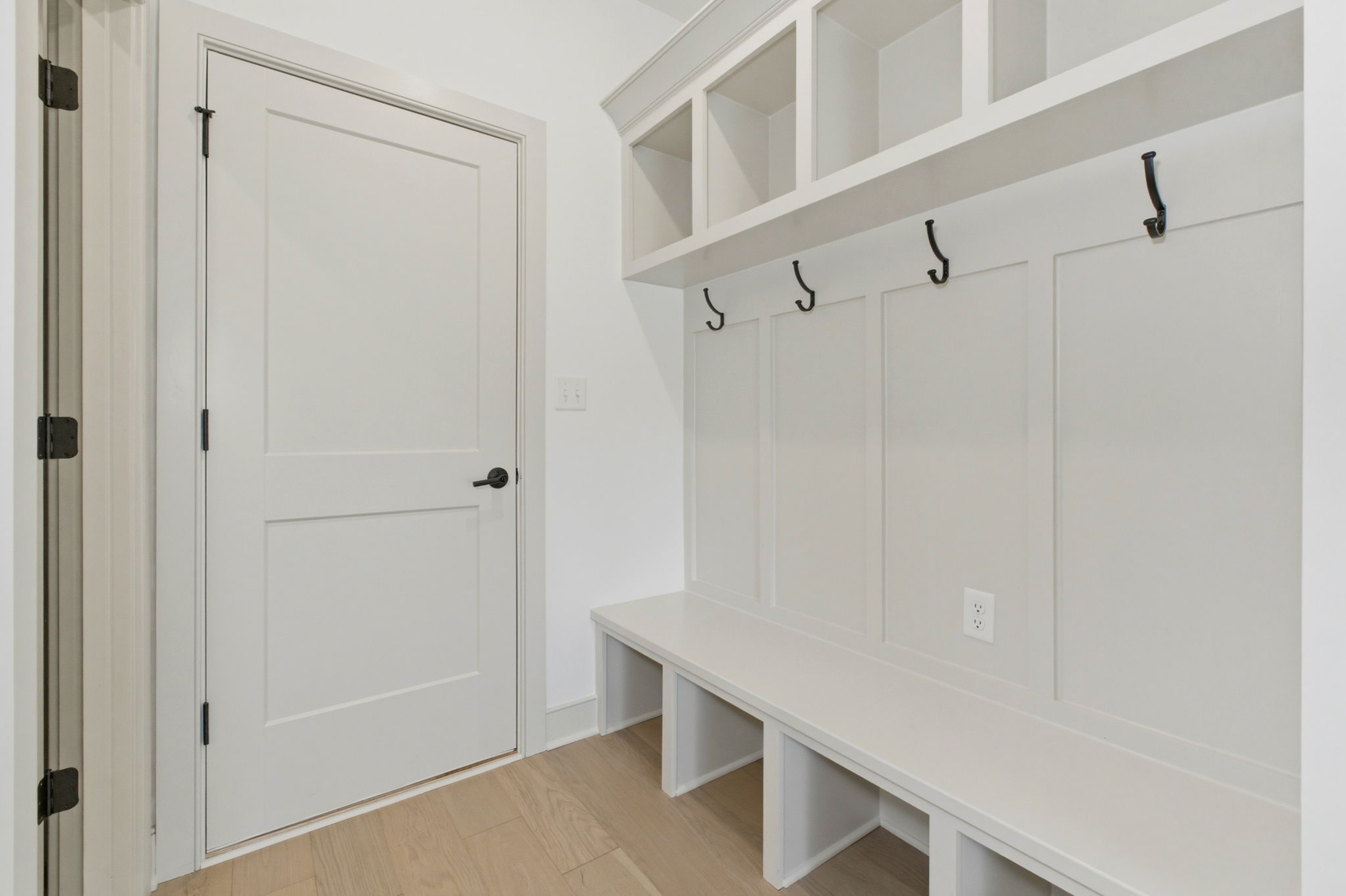 White entry nook with a built-in bench, beadboard wall, five coat hooks, and wall cubbies above the bench.