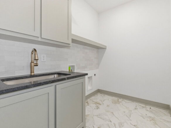 Modern laundry room with white cabinets and marble flooring.