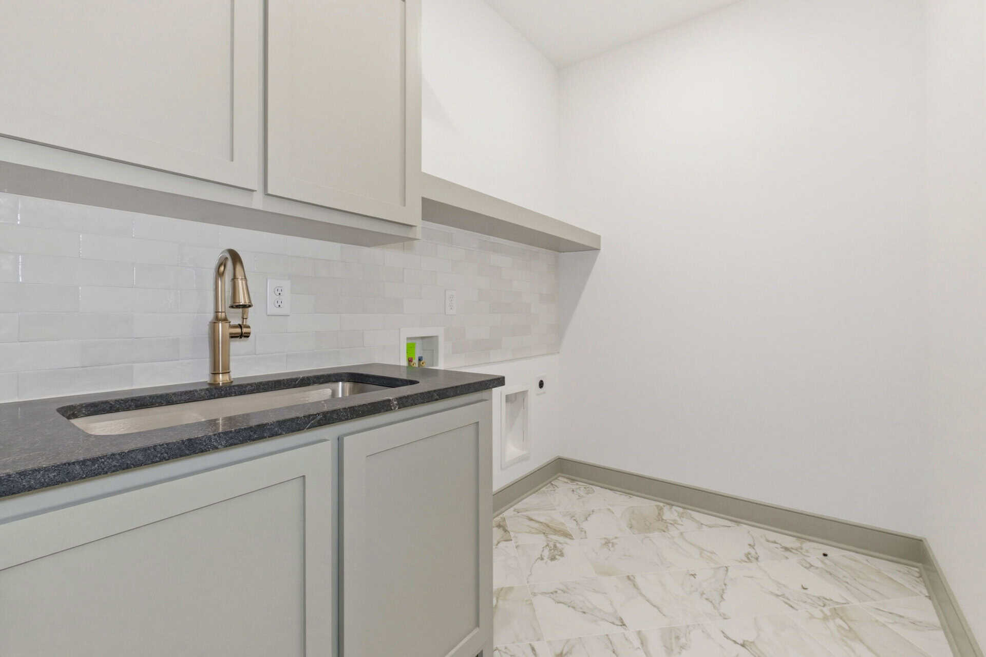 Modern laundry room with white cabinets and marble flooring.