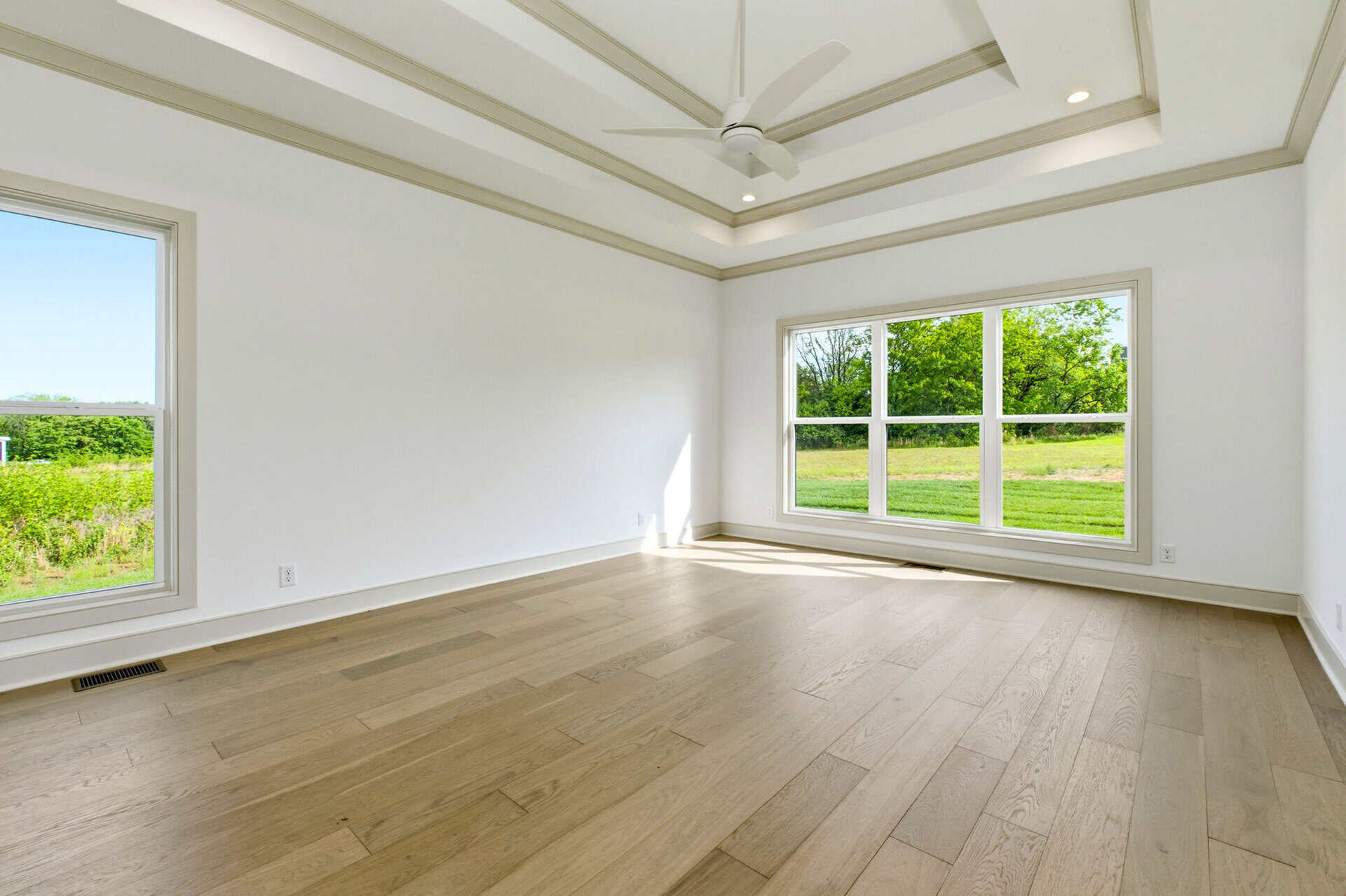Spacious empty room with large windows and hardwood floors in a new home.