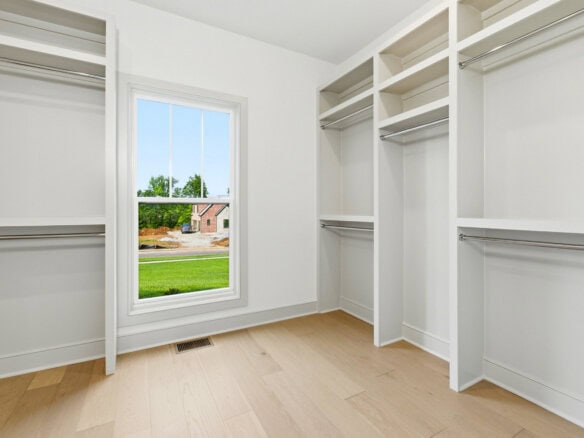 Empty walk-in closet with white shelves and a window showing a green yard.