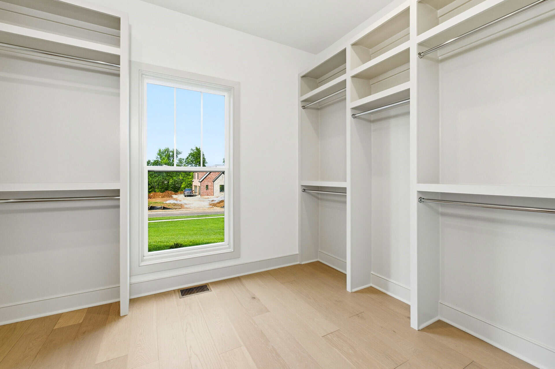 Empty walk-in closet with white shelves and a window showing a green yard.