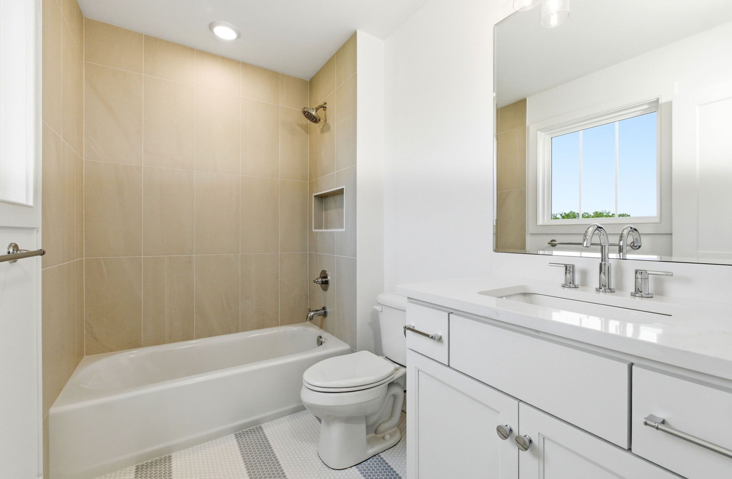 Bright white bathroom with a bathtub and beige tiled shower surround, and a white vanity beneath a window. (Informative)