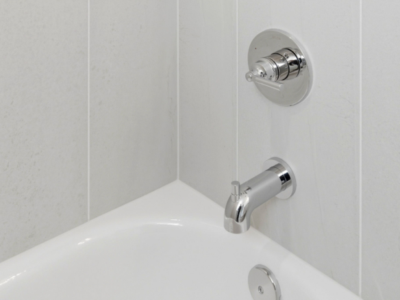 Chrome bathroom faucet and circular shower mixer on a light tiled wall above a white sink basin.