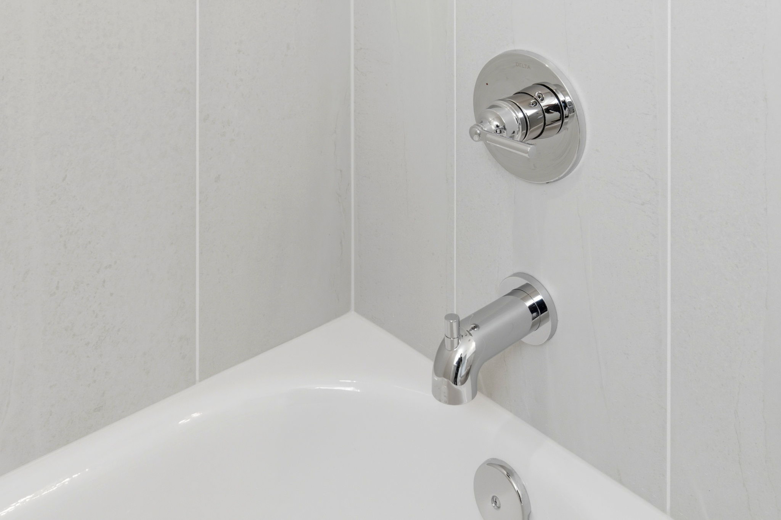Chrome bathroom faucet and circular shower mixer on a light tiled wall above a white sink basin.