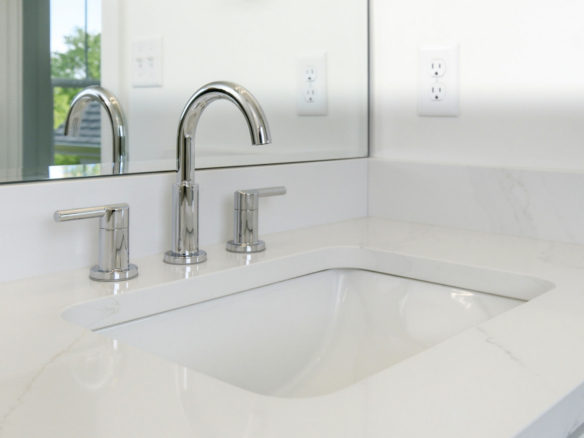 White bathroom vanity with three chrome faucets on a marble countertop and a mirror above it for a bright, clean look.