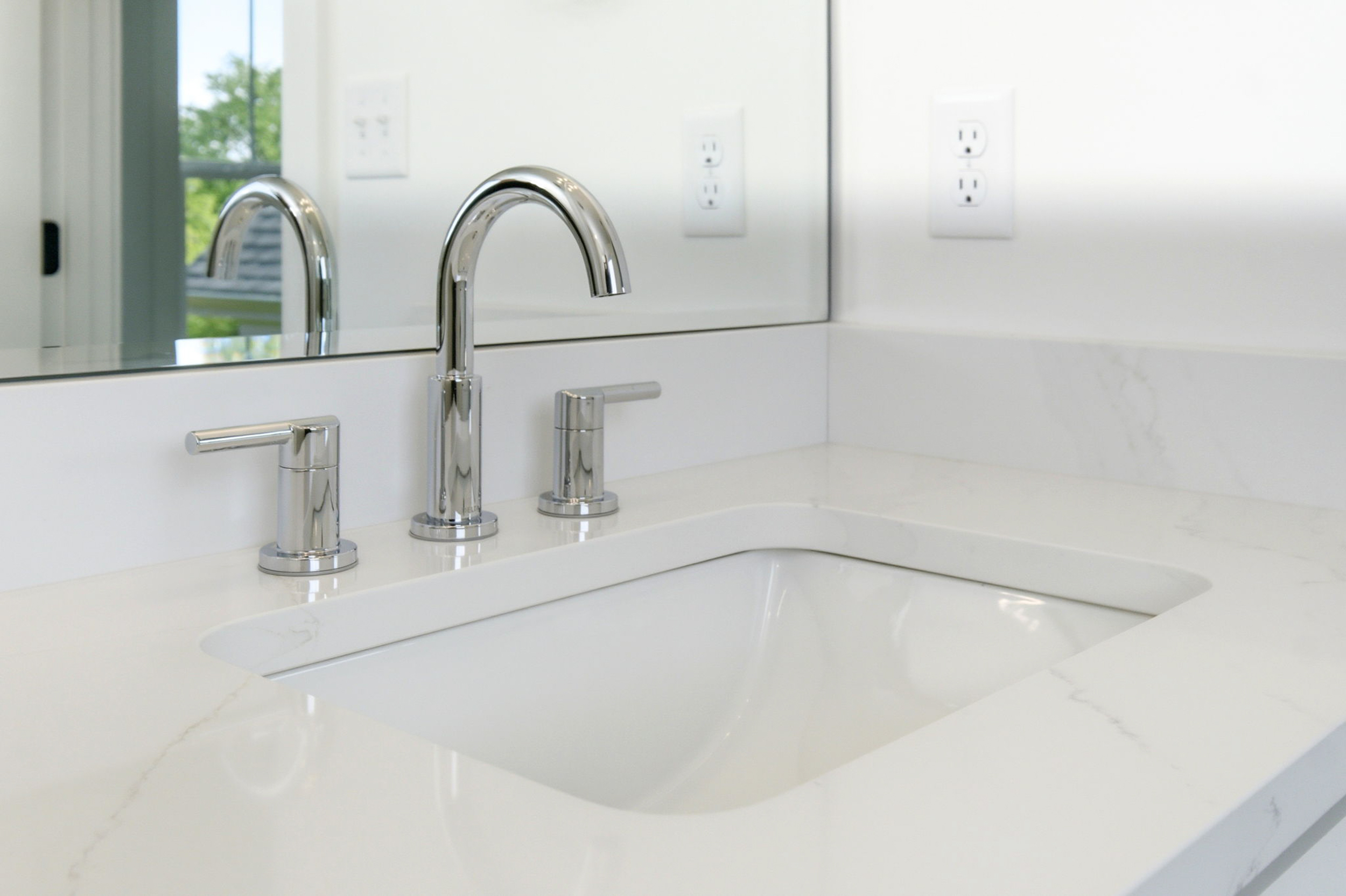 White bathroom vanity with three chrome faucets on a marble countertop and a mirror above it for a bright, clean look.