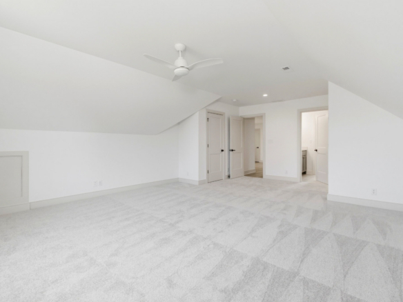 Bright empty attic bedroom with white walls and a white ceiling fan, open closet/doorways visible in the background.