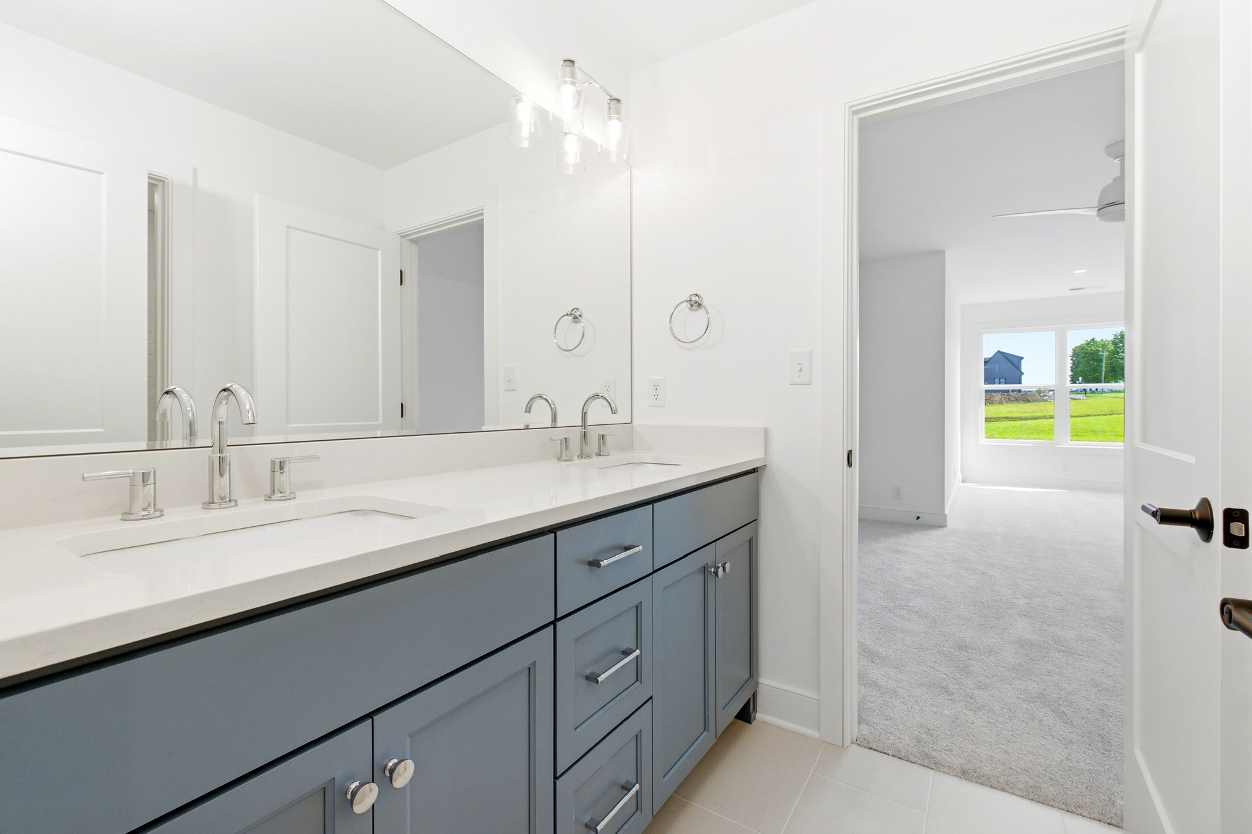 Modern bathroom with white countertops, dual sinks, and blue-gray cabinets beneath a large mirror.