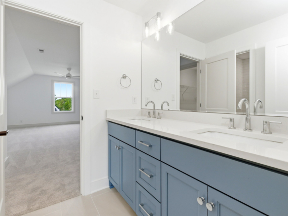 Double-sink bathroom vanity with blue cabinets, chrome faucets, and a large mirror in a bright, modern bathroom.