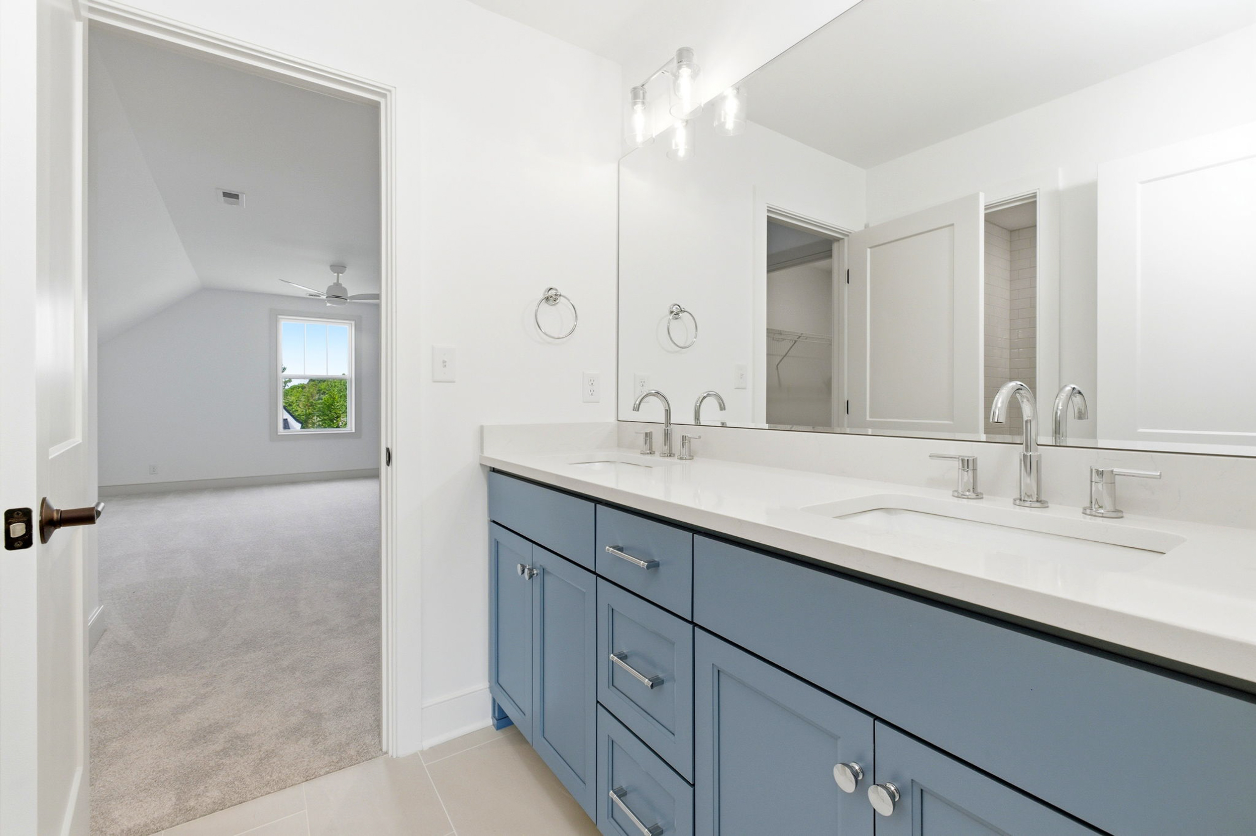 Double-sink bathroom vanity with blue cabinets, chrome faucets, and a large mirror in a bright, modern bathroom.