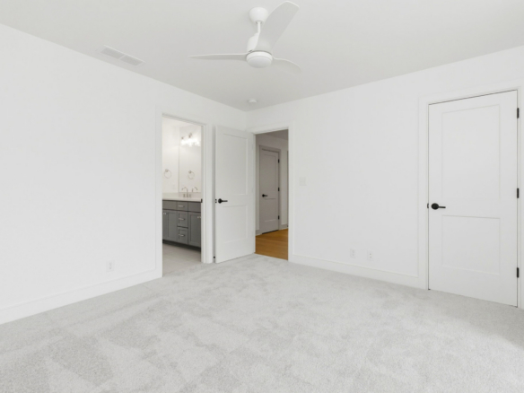 Bright white bedroom with two open doors; bathroom with grey vanity visible on the left and a white ceiling fan overhead.