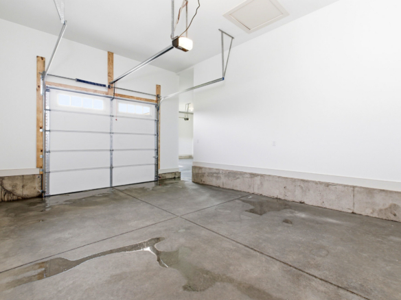 Empty residential garage with a white sectional door, concrete floor, and water stains along the baseboard area.