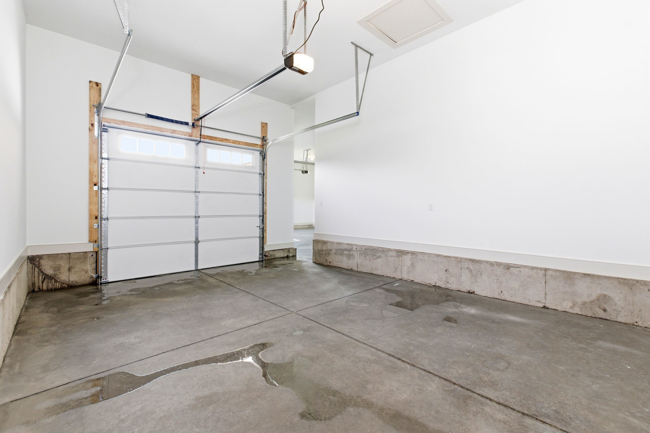 Empty residential garage with a white sectional door, concrete floor, and water stains along the baseboard area.