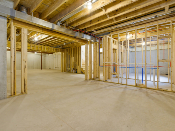 Open unfinished basement construction with wooden studs, exposed beams, and utility pipes running along the ceiling