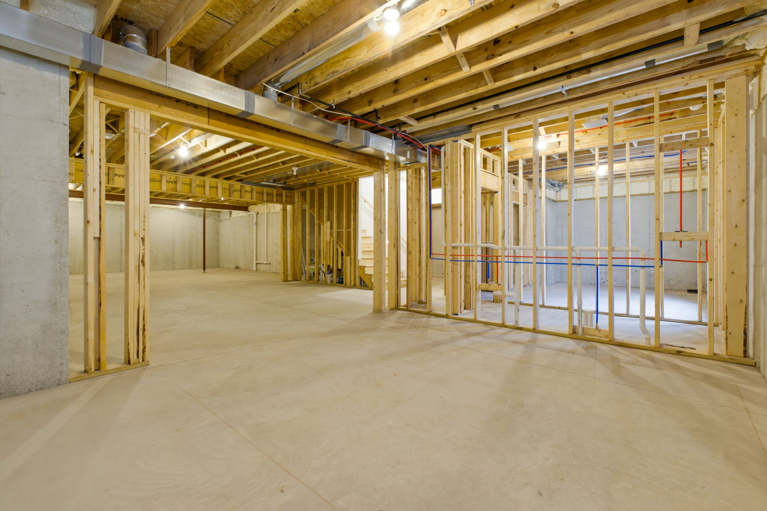 Open unfinished basement construction with wooden studs, exposed beams, and utility pipes running along the ceiling