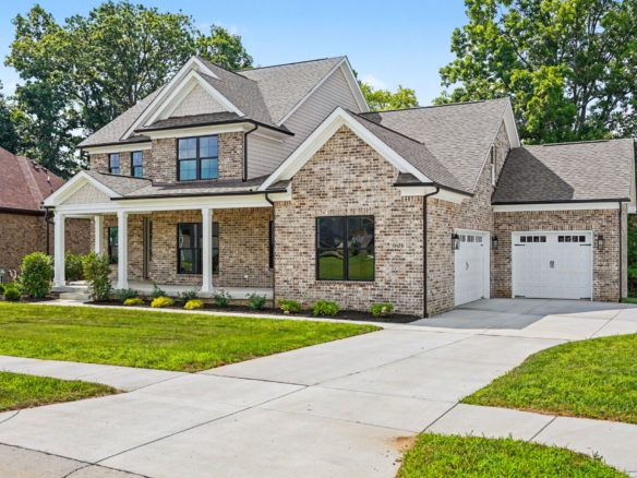 Brick two-story house with a two-car garage, front porch, and manicured lawn under a blue sky.