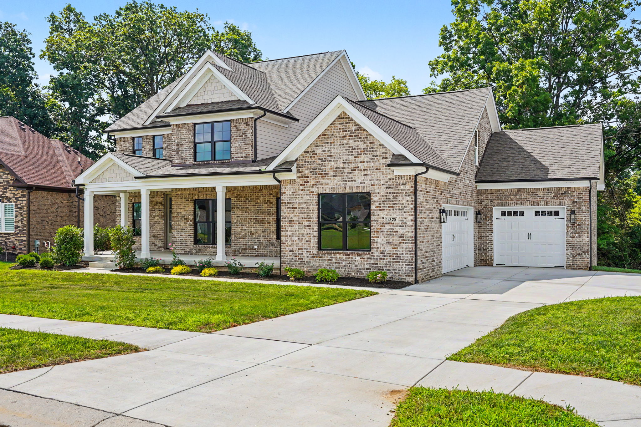 Brick two-story house with a two-car garage, front porch, and manicured lawn under a blue sky.